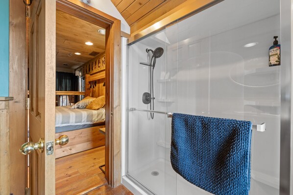 Un interior de madera con cabina de ducha de vidrio y cama con toalla azul.