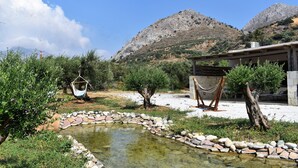Entorn exterior tranquil amb una petita bassa, un camí de pedra i una cadira espanyola.