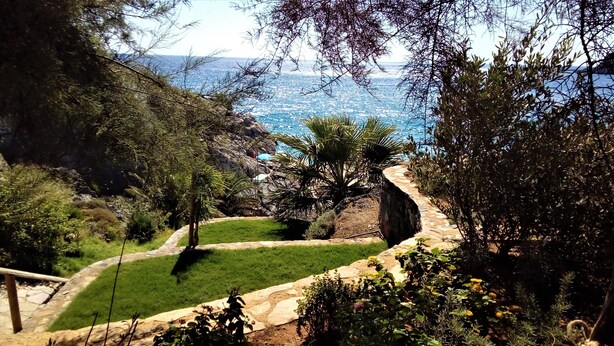 Jardí paisatjístic amb un camí de pedra, vegetació exuberant i vista al mar.