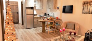 A modern kitchen with a dining area, a TV mounted on the wall, and a Christmas tree with lights.