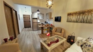 A modern living room with a glass coffee table, a sofa, and a chair. There is a kitchen in the background with a refrigerator, stove, and sink. - Apartment Levante, Carefree stay on a private farm, 1 km away from the beach (Lefkogia Rethymno)