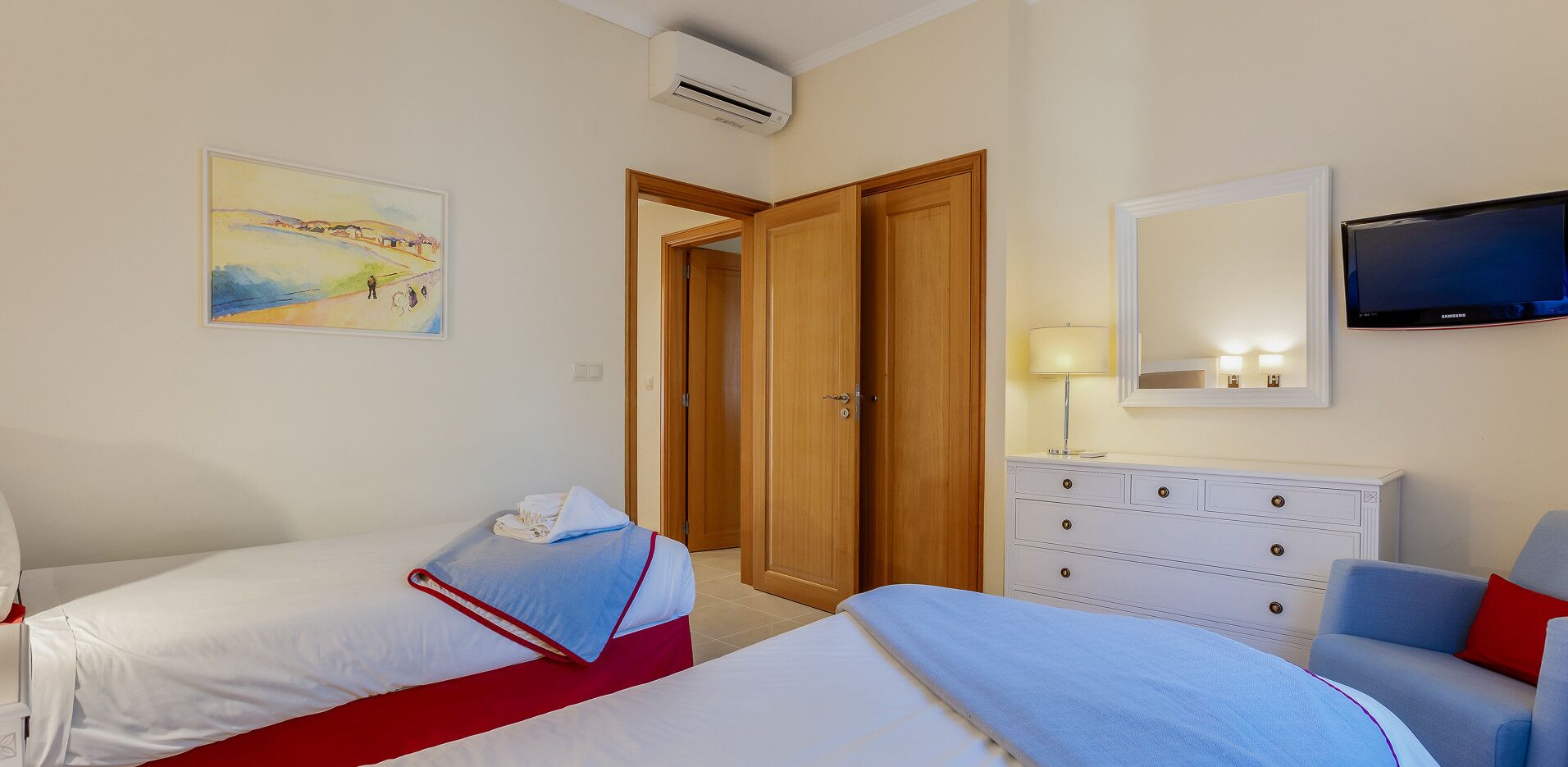 A hotel room with two beds, a TV, a dresser, and a painting on the wall.