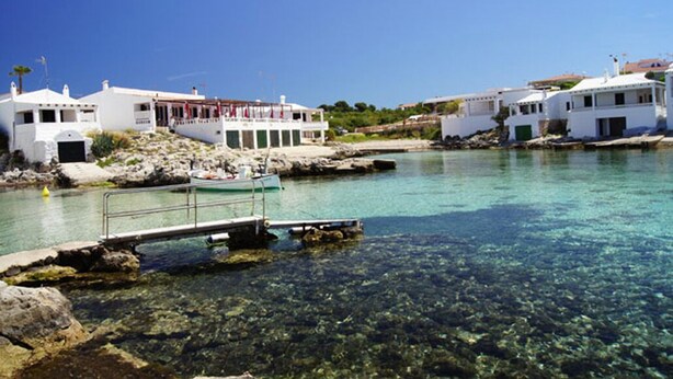 A coastal scene with clear waters, white buildings, and a dock with a boat. - Enchanting fisherman’s cottage in front of the sea in Biniancolla (Biniancolla)