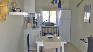 A compact kitchen with white cabinets, a dining table with blue chairs, and a hanging blue pendant light. - Enchanting fisherman’s cottage in front of the sea in Biniancolla (Biniancolla)