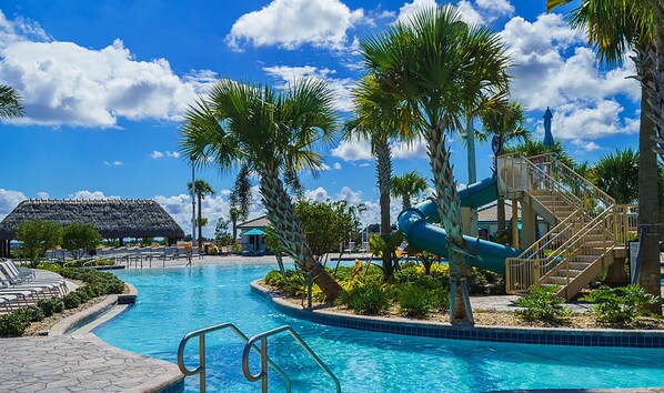 Relax by the resort pool, featuring a large pool with a slide and waterfall, surrounded by lounge chairs and umbrellas.