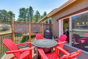 A deck with a round table and red chairs, a grill, and a view of the surrounding trees. - Newly Built Estes Park Townhome, 2 Miles to RMNP! (Estes Park)