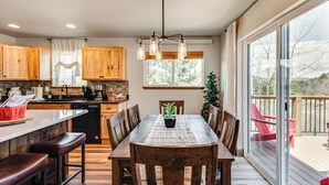 A kitchen with wooden cabinets, a dining table with chairs, a potted plant, and a view of the outdoors through large windows. - Newly Built Estes Park Townhome, 2 Miles to RMNP! (Estes Park)