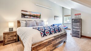 A bedroom with a wooden bed frame, a large window, and a wall-mounted air conditioning unit. - Newly Built Estes Park Townhome, 2 Miles to RMNP! (Estes Park)