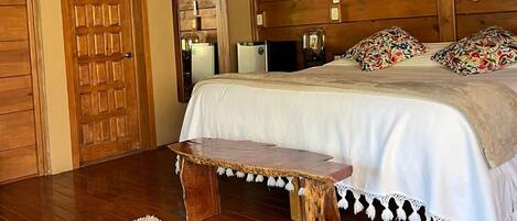 Un dormitorio acogedor con techo de madera, cama con ropa de cama blanca, un banco de madera y una alfombra blanca.