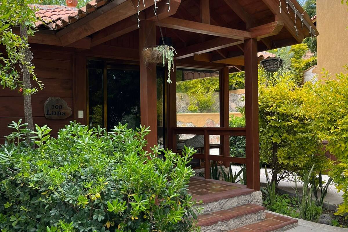 A wooden cabin with a covered porch, a stone pathway, and lush greenery.