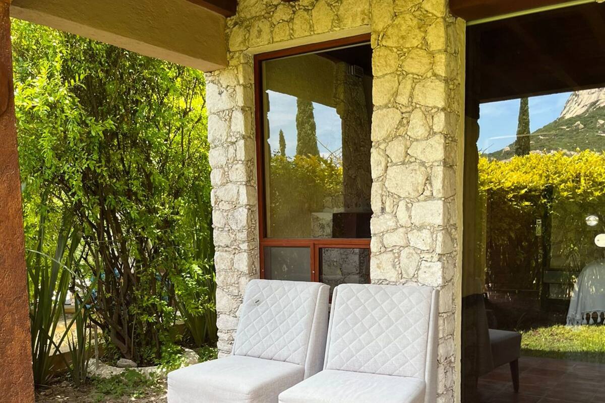 A covered patio area with two cushioned chairs and a round wooden table.