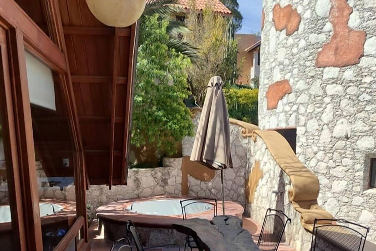 An outdoor patio with a stone wall, a wooden table, and metal chairs.