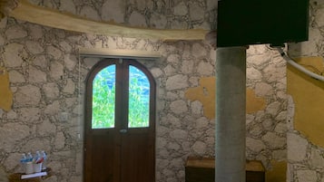 Una habitación con pared de piedra, una puerta de madera con paneles de vidrio, un televisor montado en la pared y una mesita con botellas y una taza.