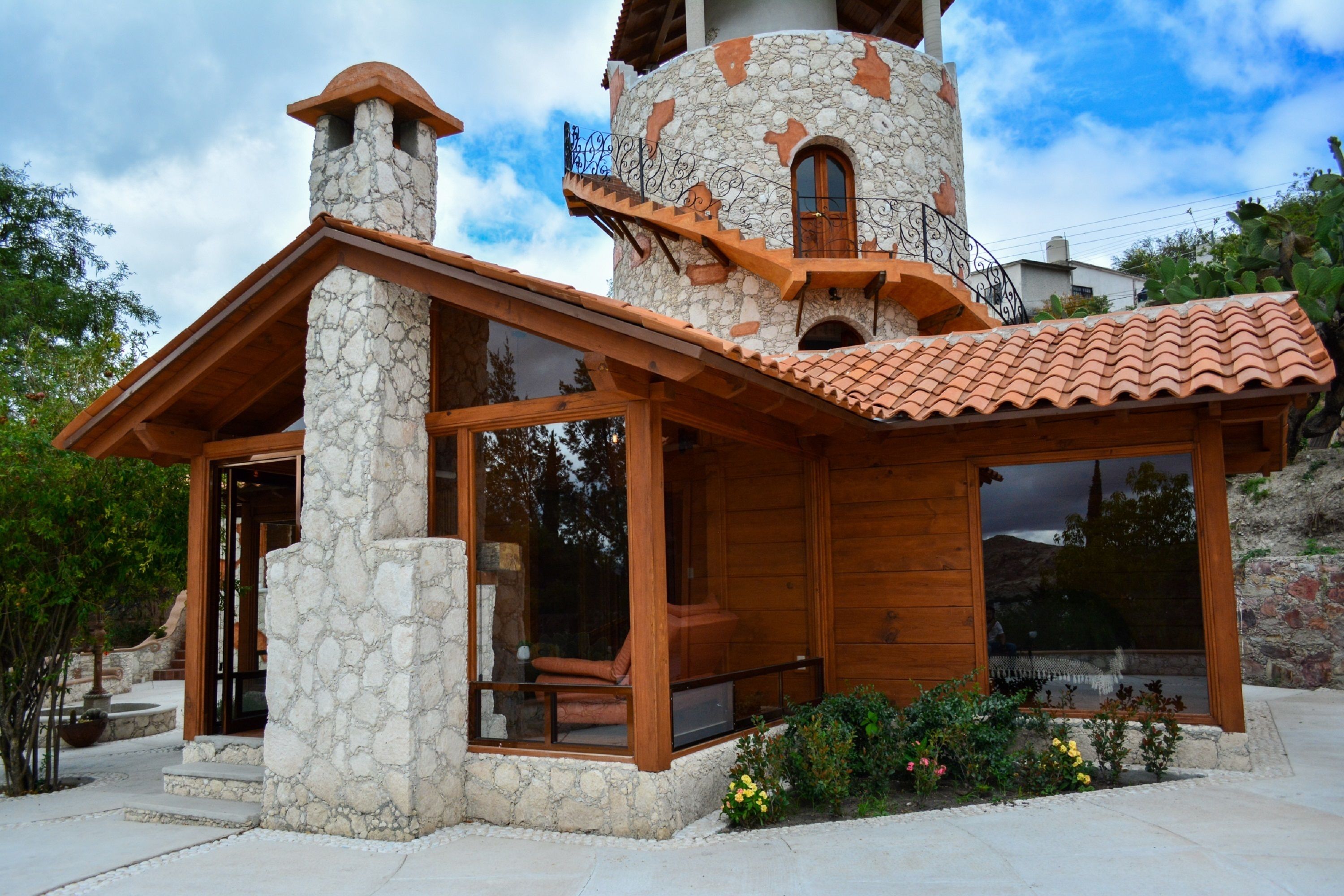 A stone and wood cabin with a chimney, large windows, and a tiled roof.