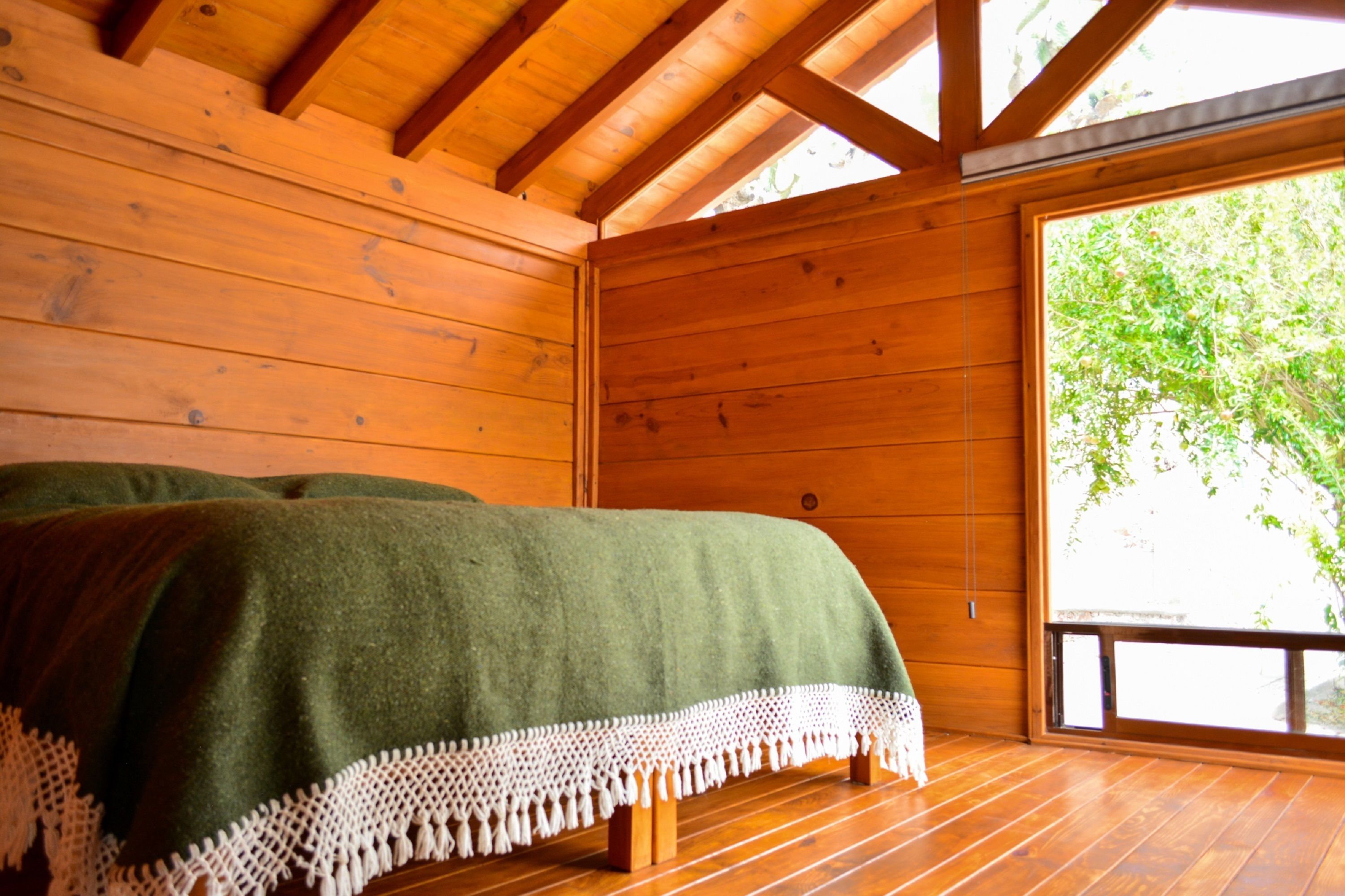 A wooden cabin room with a bed, a large window, and a view of greenery outside.