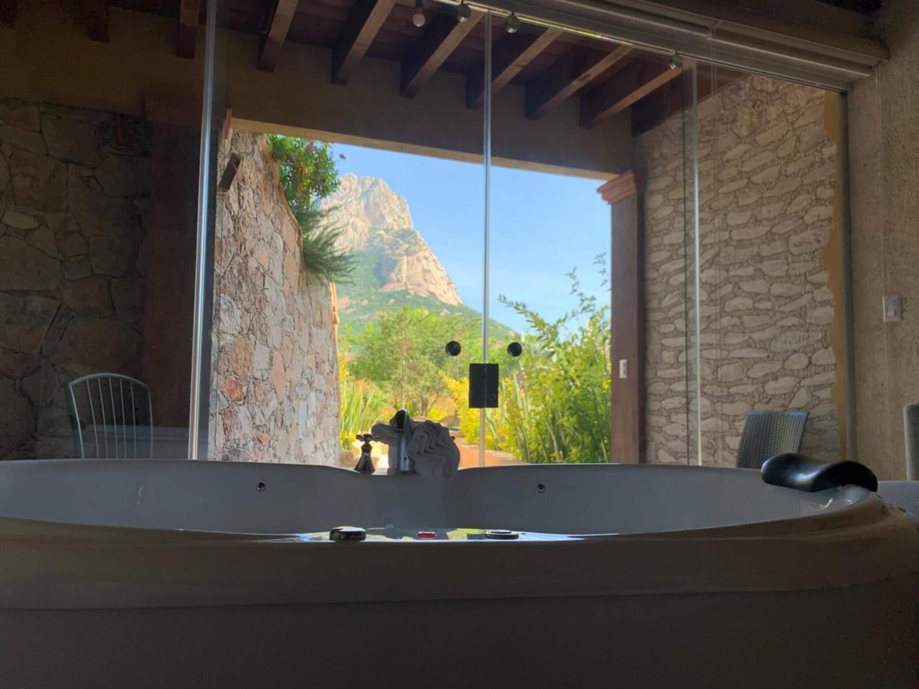 A bathroom with a bathtub, a stone wall, and a view of a mountainous landscape.