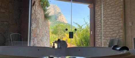 A bathroom with a bathtub, a stone wall, and a view of a mountainous landscape.