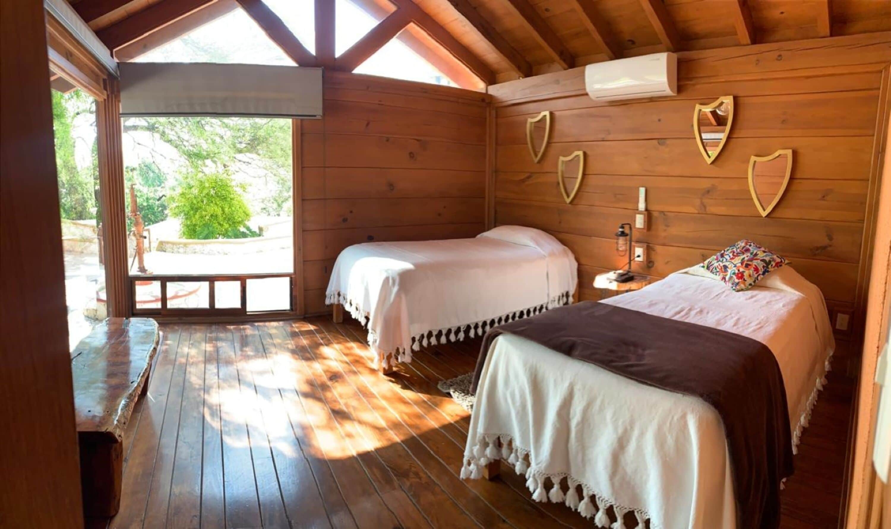 A wooden cabin with two beds, a bench, and a wooden deck.