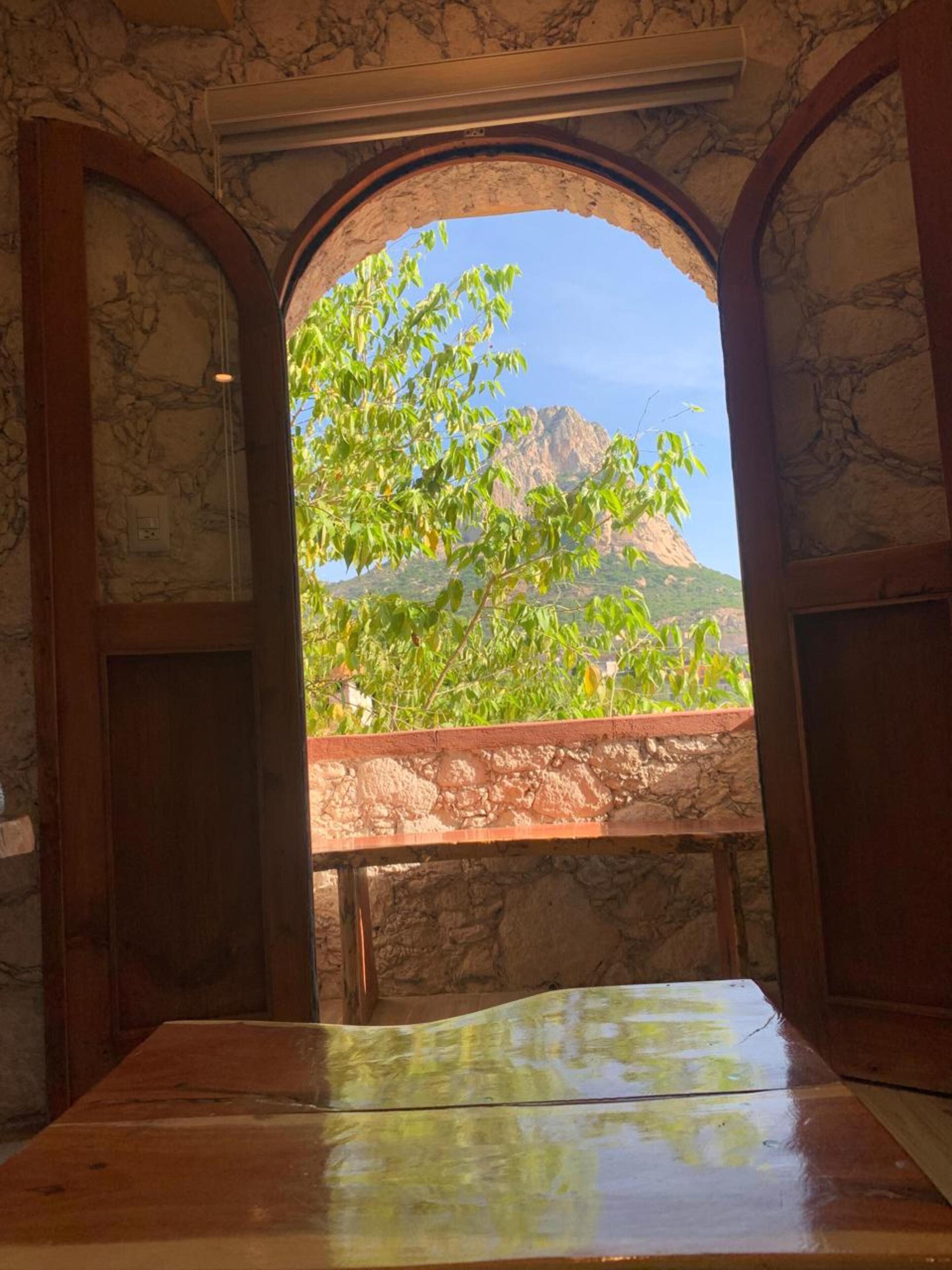 A room with a stone wall, a wooden table, and a view of a mountain through an open archway.