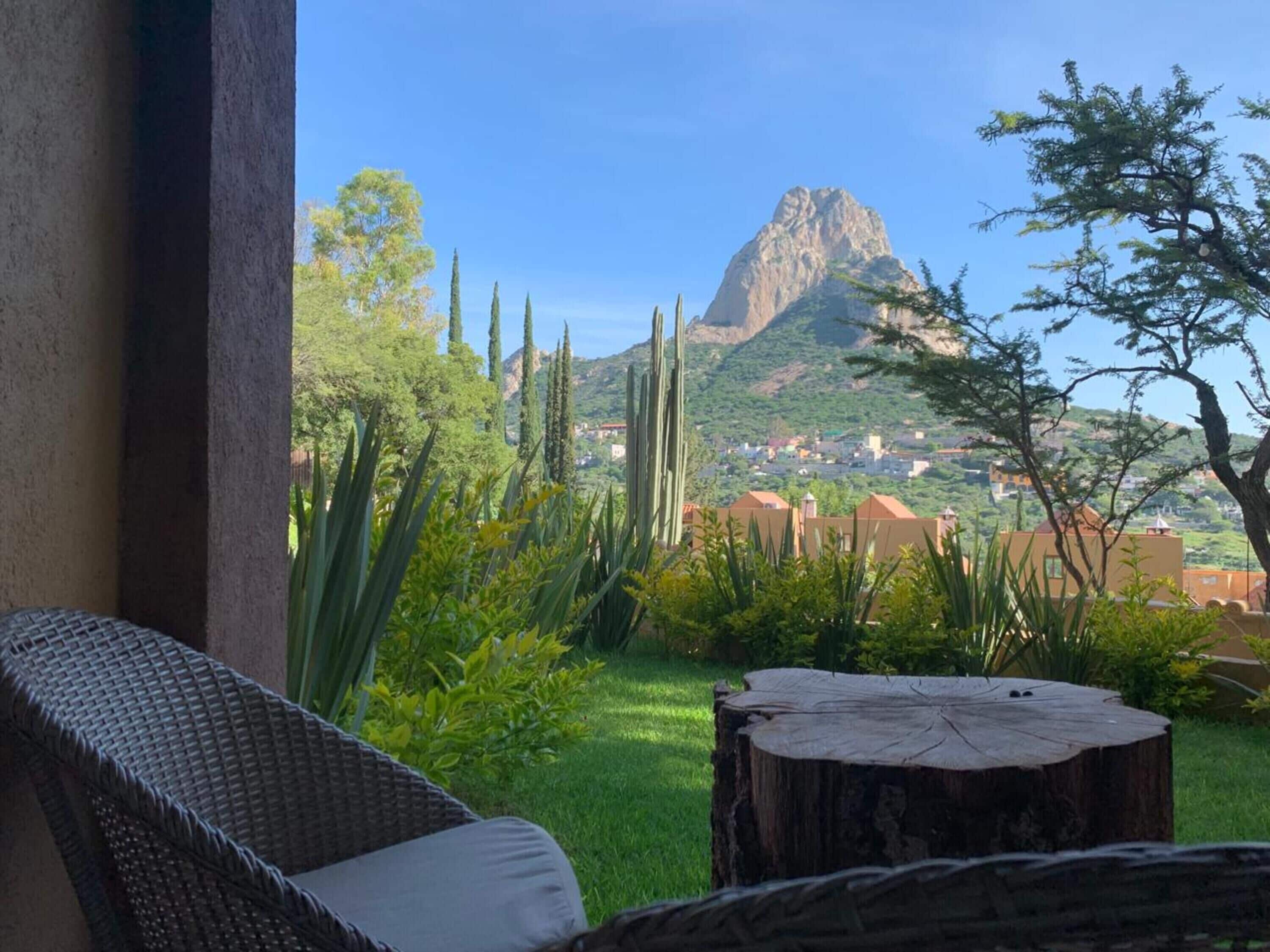 Una silla de mimbre con un cojín, un tocón de madera y una vista de una montaña y un pueblo al fondo.