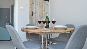 Una mesa redonda de madera con cuatro sillas grises, una botella de vino y dos copas de vino encima.