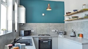 Una cocina moderna con una pared de acento color turquesa, estufa a gas, horno empotrado, microondas y tostadora.