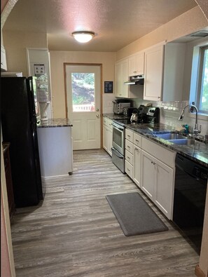 A compact kitchen with white cabinets, a black refrigerator, a built-in oven, and a sink.
