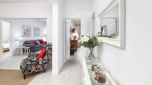 Ein modernes Wohnzimmer mit einem blumigen Sessel, einer Couch mit roten Kissen und einem Essbereich im Hintergrund.