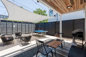 En udendørs terrasse med et pingpongbord, siddepladser og en grill.