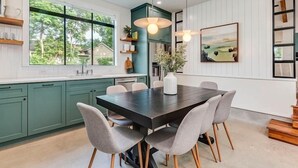A modern kitchen with teal cabinets, a dark wooden dining table, and grey upholstered chairs. - Modern Farmhouse with Rooftop Deck Downtown (Austin)
