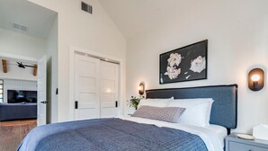 A bedroom with a large bed, a bedside table, a wall-mounted light, and a door leading to another room. - Modern Farmhouse with Rooftop Deck Downtown (Austin)