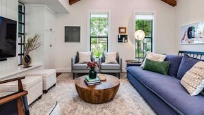 A spacious living room with a high ceiling, a blue sofa, a grey armchair, and a round wooden coffee table. - Modern Farmhouse with Rooftop Deck Downtown (Austin)