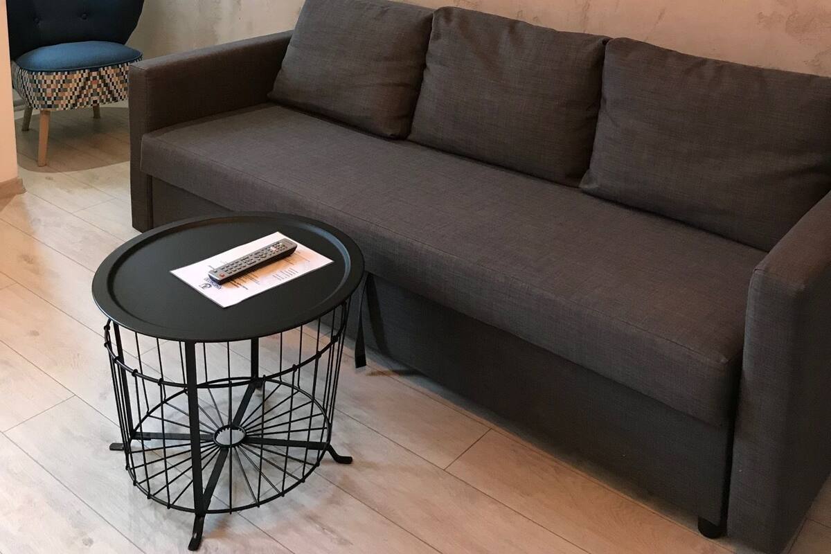 Ein modernes Wohnzimmer mit einem grauen Sofa, einem runden schwarzen Couchtisch und einem blauen Sessel. An der Wand hängt ein großes abstraktes Gemälde.