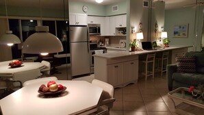 Et moderne køkken med hvide skabe, et køleskab, en mikrobølgeovn og et spiseområde med et bord og stole.