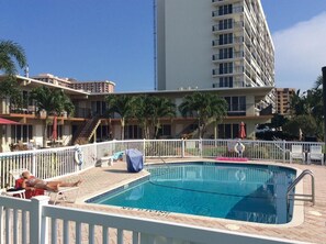 Una piscina amb una tanca blanca, palmeres i un edifici alt al fons.