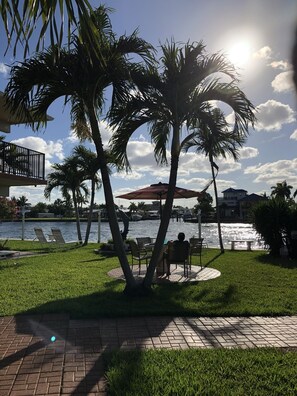 A sunny outdoor area with palm trees, a water body, and lounge chairs. - Aqua Mar Condos (Pompano Beach)