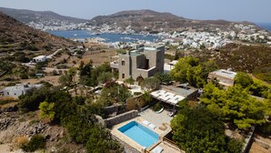 Une propriété située sur la côte, dotée d’une piscine, d’une architecture en pierre et offrant une vue sur une ville et la mer.
