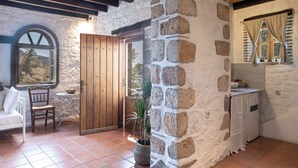 Une pièce rustique avec un mur en pierre, une porte en bois, un sol carrelé et une petite table accompagnée d’une chaise.