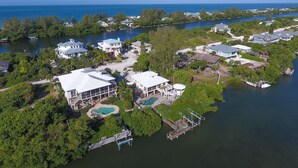 An aerial view of a coastal residential area with houses, a dock, and a swimming pool.