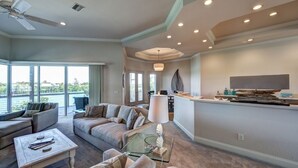 A spacious living room with a large sofa, a coffee table, and a TV area with a flat-screen TV and decorative items.