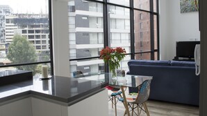 A modern apartment with a kitchen area, a dining table with chairs, a sofa, and a large window offering a view of a cityscape. - SENSATIONAL APARTMENT FOR COUPLES/EXECUTIVES/SHORT FAMILY (Quito)