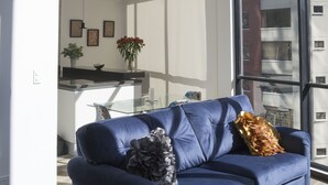 A modern living room with a blue sofa, a glass balustrade, and a view of the cityscape through large windows. - SENSATIONAL APARTMENT FOR COUPLES/EXECUTIVES/SHORT FAMILY (Quito)