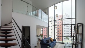 A modern apartment with a staircase, a living area with a sofa, a dining table, and large windows offering a city view. - SENSATIONAL APARTMENT FOR COUPLES/EXECUTIVES/SHORT FAMILY (Quito)