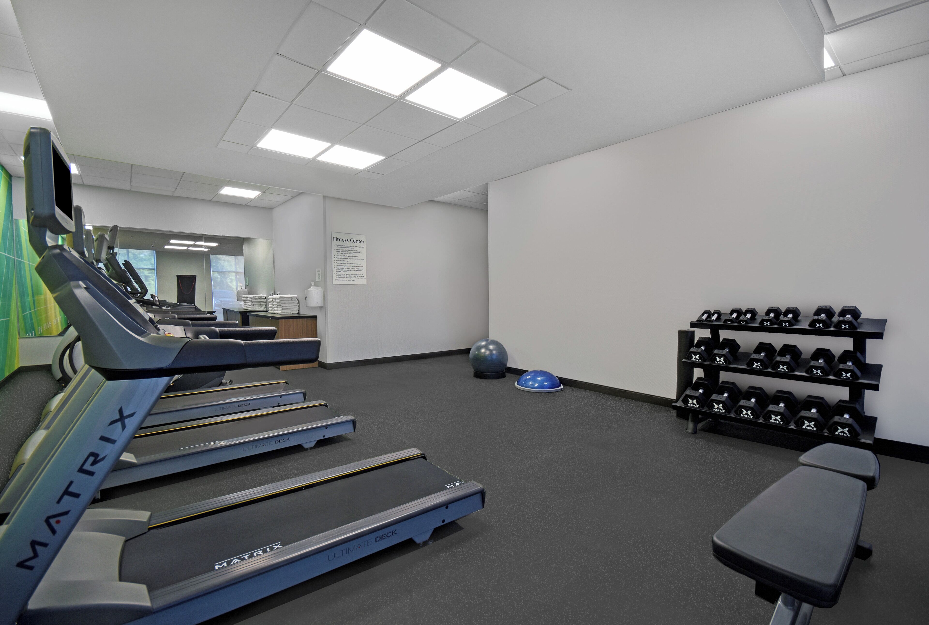 Et fitnesscenter med løbebånd, en bænk og et stativ med håndvægte.