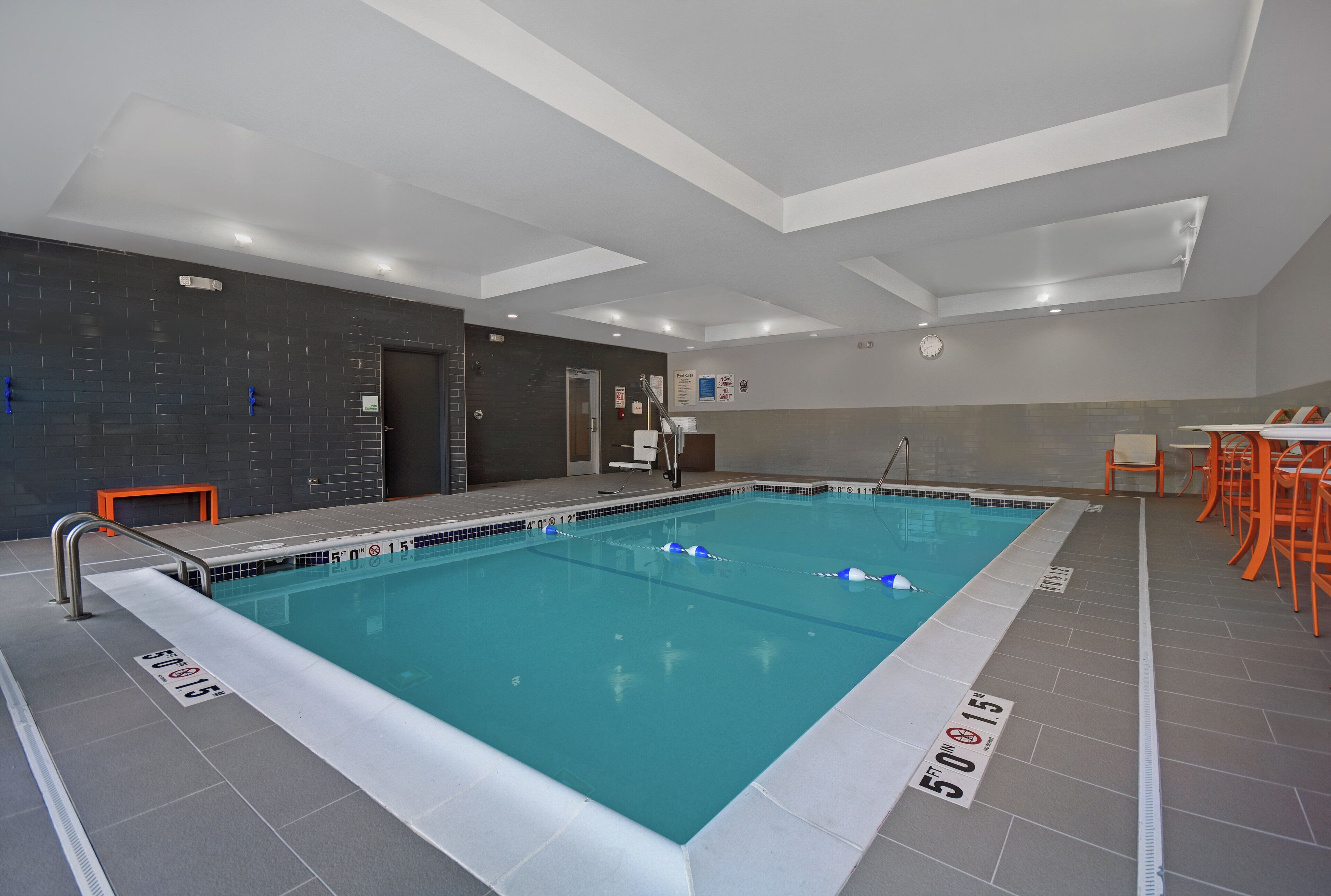 An indoor swimming pool with clear lane markings, a safety sign, and a clock on the wall.