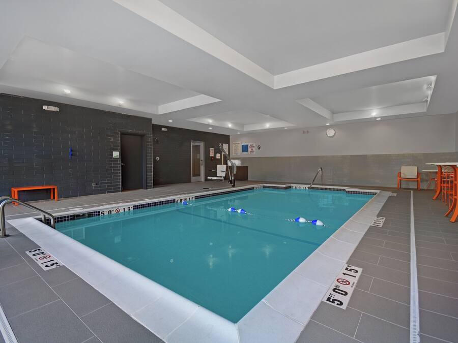 Una piscina interior amb marques clares per carrils, un senyal de seguretat i un rellotge a la paret.
