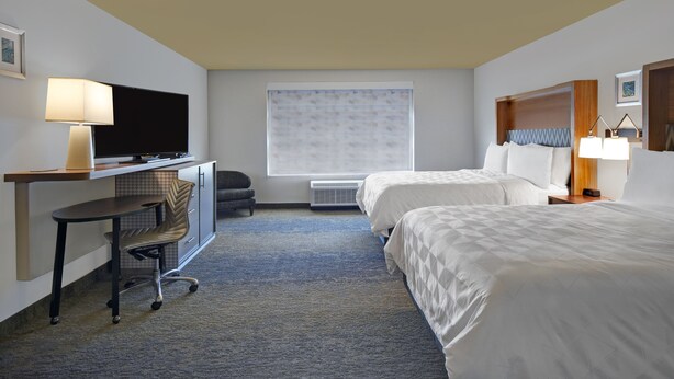 A hotel room with a desk, two beds, a TV, and a window with blinds. - Holiday Inn Grand Rapids North - Walker by IHG (Grand Rapids)
