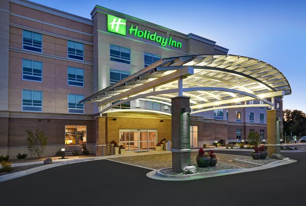Un hotel Holiday Inn con entrada cubierta, varios pisos y una zona ajardinada con plantas.