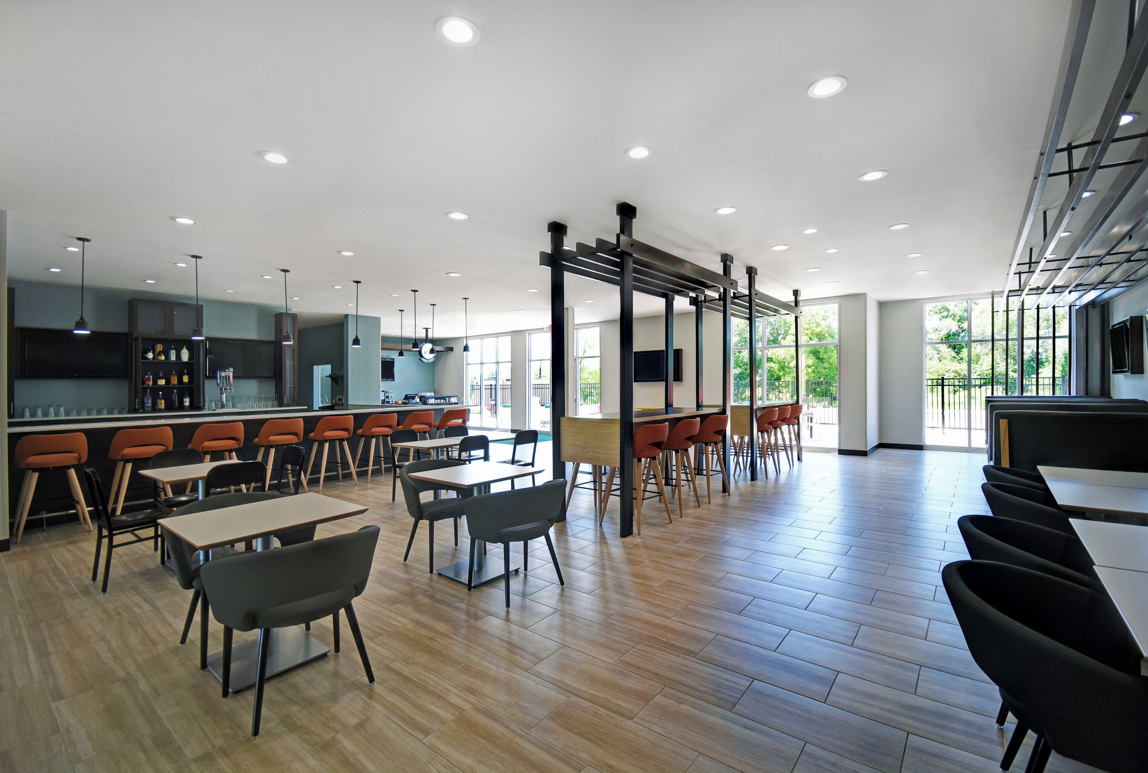 Un espacio interior amplio con varios conjuntos de asientos, incluyendo mesas y sillas, y una zona de bar con taburetes.