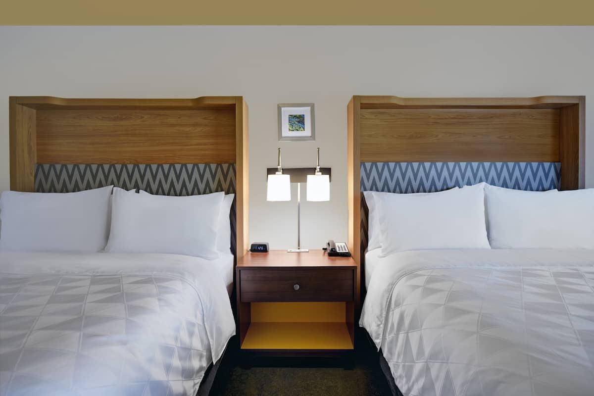 Une chambre d’hôtel avec deux lits, une table de chevet avec une lampe, un téléphone et un tableau encadré au mur.